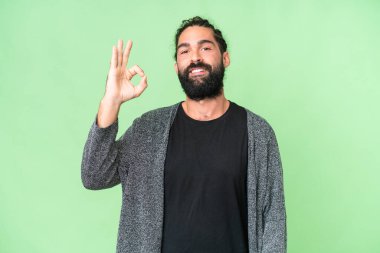 Sakallı genç adam izole edilmiş krom anahtar arka planda parmaklarıyla işaret gösteriyor.