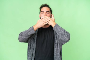 Sakallı genç adam izole edilmiş krom arka planda ağzı elleriyle kapatıyor.