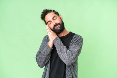 Sakallı genç bir adam izole edilmiş krom anahtar arkaplanda uyku jesti yapıyor.