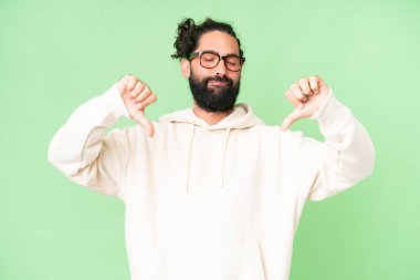 Young man with beard over isolated chroma key background showing thumb down with two hands