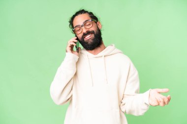 Young man with beard over isolated chroma key background keeping a conversation with the mobile phone with someone