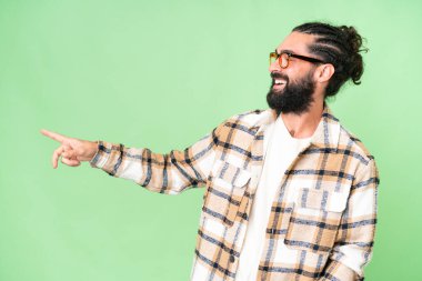 Young man with beard over isolated chroma key background pointing finger to the side and presenting a product