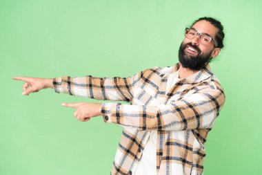 Young man with beard over isolated chroma key background pointing finger to the side and presenting a product