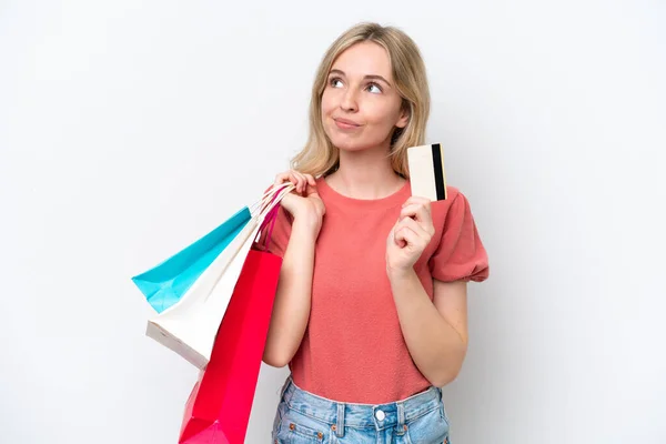 白い背景に隔離された若い英語の女性ショッピングバッグとクレジットカードと思考を保持 — ストック写真