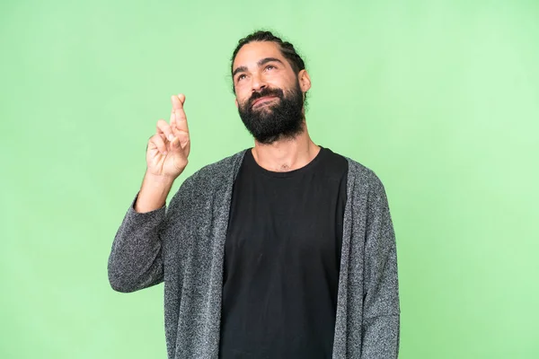Young man with beard over isolated chroma key background with fingers crossing and wishing the best