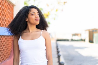 Genç Afro-Amerikalı kadın açık havada, kafası karışmış bir yüz ifadesi var.