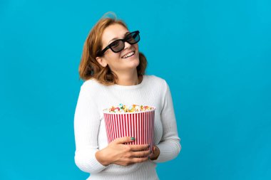 Genç Gürcü kadın mavi arka planda gözlüklü ve elinde koca bir kova patlamış mısır tutuyor.