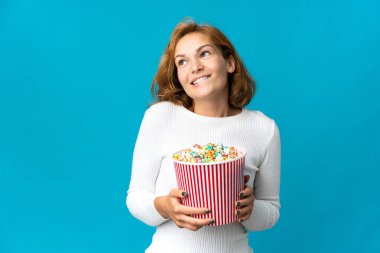 Genç Gürcü bir kadın mavi arka planda izole edilmiş. Elinde koca bir kova patlamış mısır var.