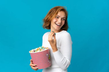 Genç Gürcü bir kadın mavi arka planda izole edilmiş. Elinde koca bir kova patlamış mısır var.