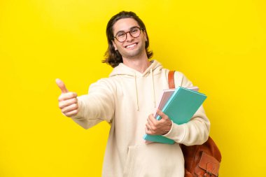 Young student handsome man isolated on yellow background giving a thumbs up gesture