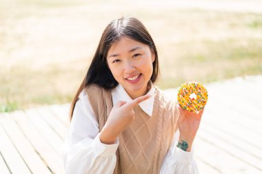 Genç Çinli bir kadın açık havada bir çörek tutuyor ve ona doğrultuyor.