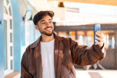 Açık havada yakışıklı bir Arap cep telefonuyla selfie çekiyor.