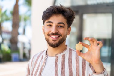 Açık havada Bitcoin tutan yakışıklı bir Arap.