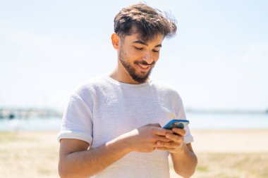 Dışarıdaki yakışıklı Arap cep telefonuyla mesaj yolluyor.