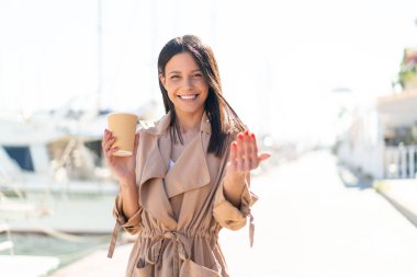 Dışarıdaki genç bir kadın açık havada kahvesini yudumluyor ve benimle gelmesi için davet ediyor. Gelmene sevindim.