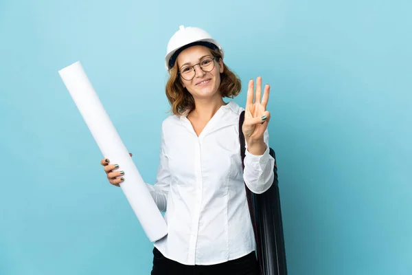 Young architect Georgian woman with helmet and holding blueprints over isolated background happy and counting three with fingers