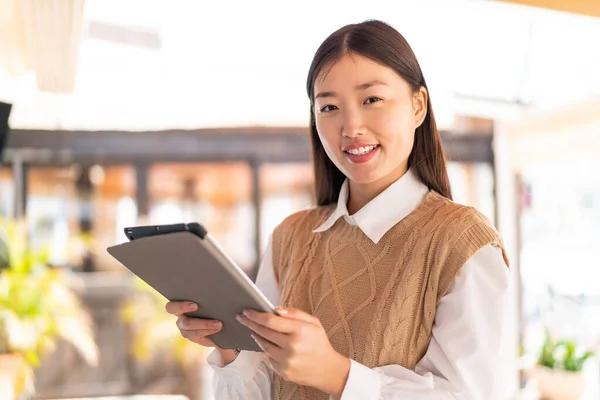 stock image Young Chinese woman at outdoors holding a tablet with happy expression