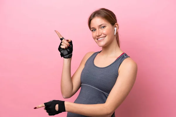 ピンクの背景に指を向けて製品を提示し 若いスポーツの白人女性が孤立 — ストック写真
