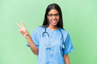 Genç Afrikalı Amerikalı hemşire, izole edilmiş arka planda gülümsüyor ve zafer işareti gösteriyor.