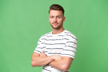 Sarışın, beyaz, soyutlanmış, kolları çapraz ve ileriye bakan bir adam.