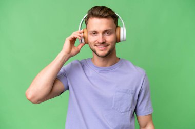 İzole edilmiş arka planda genç sarışın beyaz adam müzik dinliyor.