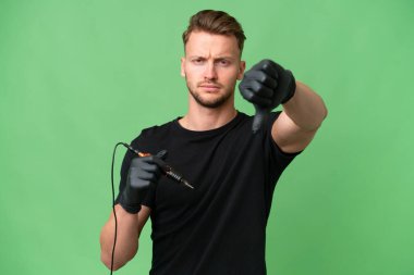 Dövme sanatçısı Kafkasyalı, izole edilmiş arka planda, olumsuz ifadeyle baş parmağını aşağı gösteriyor.