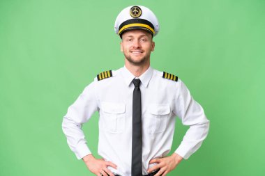 Uçak pilotu izole edilmiş arka planda kolları kalçasında ve gülümsüyor.