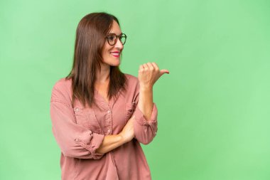 İzole edilmiş geçmişi olan orta yaşlı beyaz bir kadın bir ürünü sunmak için kenarı işaret ediyor.