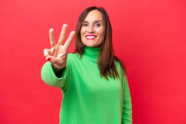 Orta yaşlı beyaz kadın kırmızı arka planda izole edilmiş mutlu ve parmaklarıyla üçe kadar sayıyor.