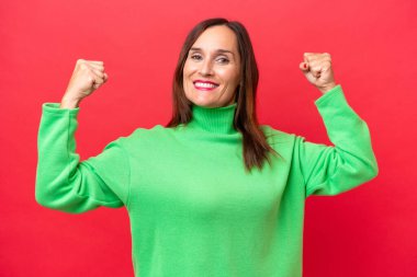 Orta yaşlı beyaz kadın, kırmızı arka planda izole edilmiş, güçlü bir jest yapıyor.