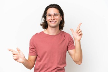 Beyaz arka planda izole edilmiş genç yakışıklı adam parmak uçlarını işaret ediyor ve mutlu.