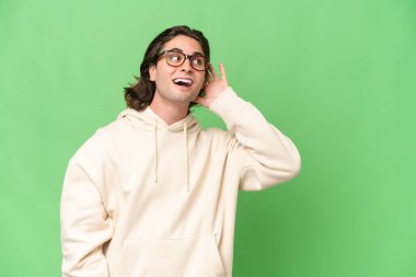 Genç beyaz adam yeşil krom arka planda izole edilmiş. Kulağına elini sürerek bir şeyler dinliyor.