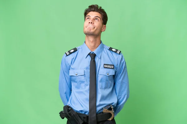 Young police man over isolated background and looking up