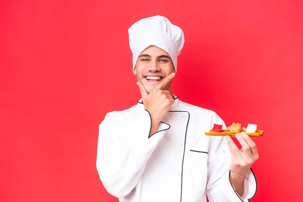 赤い背景に孤立した刺身を持つ若い白人料理人幸せと笑顔 — ストック写真