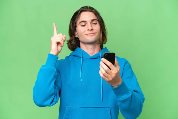 年轻英俊男子被隔离在绿色的背景下使用手机和举起手指 — 图库照片