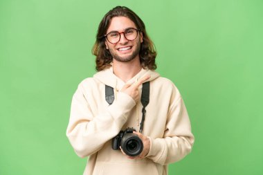 İzole edilmiş arka planda genç fotoğrafçı bir ürünü sunmak için kenarı işaret ediyor.