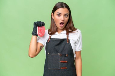 Butcher woman wearing an apron and serving fresh cut meat isolated on green chroma background with surprise facial expression