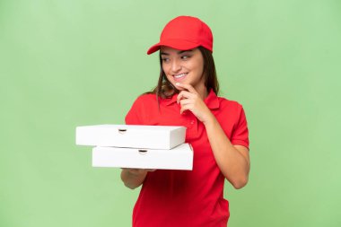 Pizza teslimatı, iş üniformalı beyaz bir kadın yeşil krom arka planda izole edilmiş pizza kutularını topluyor ve gülümsüyor.