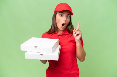 İş üniformalı beyaz bir kadın yeşil krom arka planda izole edilmiş pizza kutularını topluyor. Çözümü bulmak için parmağını kaldırıyor.
