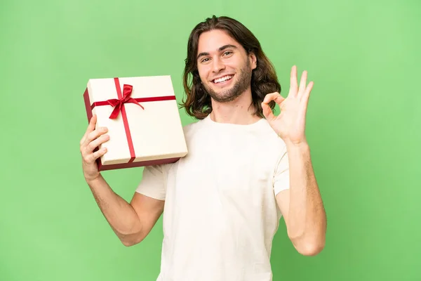 Молодой Красивый Мужчина Держит Подарок Изолированном Фоне Показывая Знак Пальцами — стоковое фото