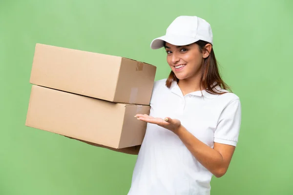 stock image Delivery caucasian woman holding boxes isolated on green chroma background extending hands to the side for inviting to come