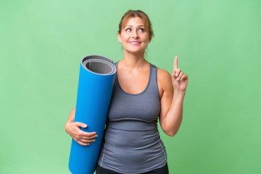 Orta yaşlı bir kadın yoga derslerine giderken elinde paspas tutarak harika bir fikre işaret ediyor.