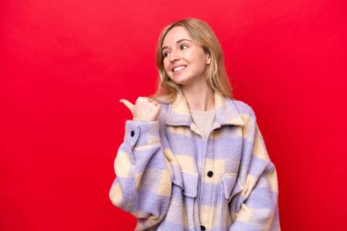 Young English woman isolated on red background pointing to the side to present a product