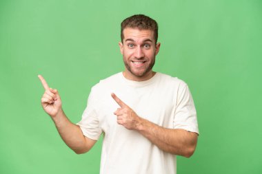 Yeşil krom arka planda izole edilmiş yakışıklı beyaz adam korkmuş ve kenarı işaret ediyor.