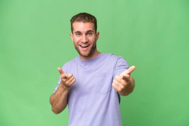 Yeşil krom arka planda izole edilmiş yakışıklı beyaz adam ön tarafı işaret ediyor ve gülümsüyor.