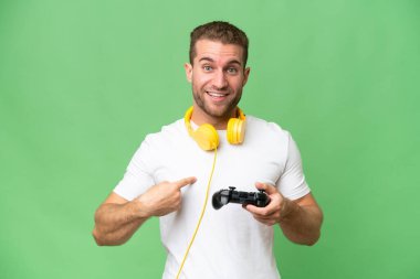 Genç yakışıklı bir adam, yeşil renkli arka planda izole edilmiş bir video oyunu kontrolörüyle oynuyor. Şaşırtıcı bir yüz ifadesi var.