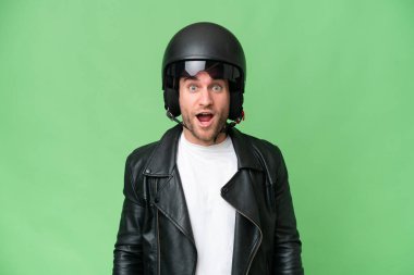 Motosiklet kasklı, yeşil renkli arka planda, şaşırtıcı bir yüz ifadesi olan beyaz bir genç.