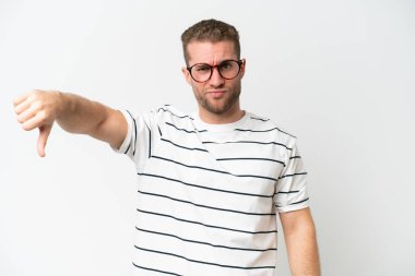 Beyaz arka planda izole edilmiş beyaz, yakışıklı beyaz bir adam, olumsuz bir ifadeyle baş parmağını aşağı gösteriyor.