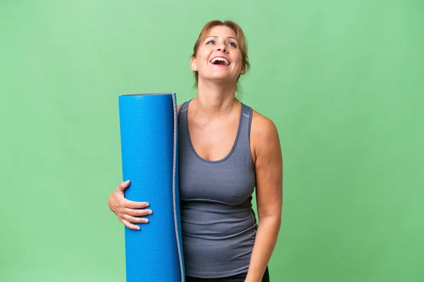 中年妇女去上瑜伽课 同时拿着垫子挡住孤立的背景笑 — 图库照片