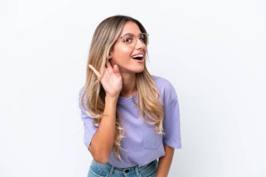 Genç Uruguaylı kadın beyaz arka planda izole edilmiş bir şekilde elini kulağına koyarak bir şeyler dinliyor.